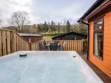 An outdoor hot tub on a wooden deck next to a table with chairs and surrounded by a wooden fence at Wansfell View in Limefitt Park near Troutbeck