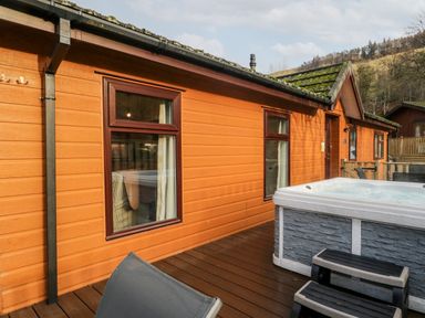 An outdoor deck with a hot tub steps and patio chairs outside a wooden cabin at Wansfell View in Limefitt Park near Troutbeck