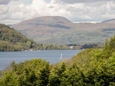 A lake surrounded by trees with hills and a sailboat in the water at Wansfell View Limefitt Park near Troutbeck