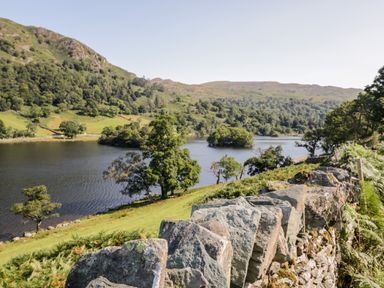 A lake surrounded by hills trees and a stone wall at Wansfell View in Limefitt Park near Troutbeck