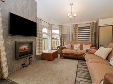 A living room with two sofas a television above a fireplace and windows with curtains at Wansfell View Limefitt Park near Troutbeck