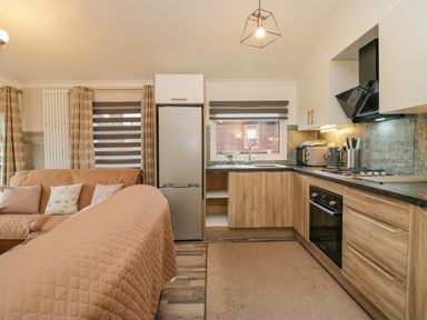 A kitchen with wooden cabinets a refrigerator an oven and a sink next to a living area with a sofa at Wansfell View in Limefitt Park near Troutbeck