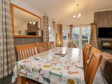 A dining area with wooden chairs and a table covered with animal print tablecloth near a window and fireplace at Wansfell View Limefitt Park near Troutbeck