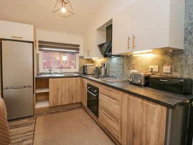 A kitchen with wood cabinets a refrigerator a sink a toaster and a stove at Wansfell View in Limefitt Park near Troutbeck