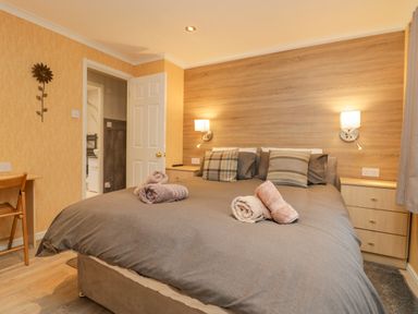 A bedroom with a double bed and rolled towels on it bedside tables wall lamps and a wooden desk at Wansfell View in Limefitt Park near Troutbeck