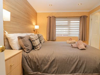 A bedroom with a bed made with pillows and towels by the window with curtains at Wansfell View Limefitt Park near Troutbeck