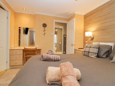 A bedroom with a bed and folded towels on it a desk with a chair and an open door leading to a bathroom at Wansfell View in Limefitt Park near Troutbeck