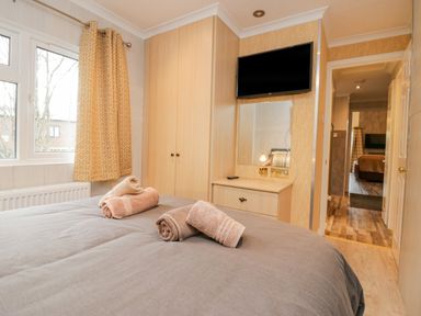 A bedroom with a bed towels on it a wardrobe a wall mounted tv and a window with patterned curtains at Wansfell View in Limefitt Park near Troutbeck