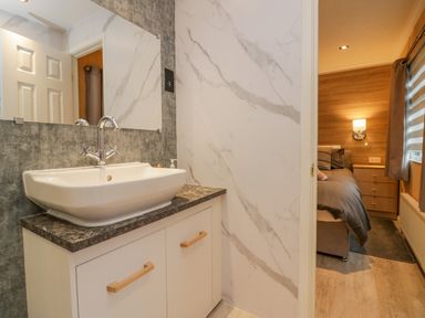 A bathroom sink with a large mirror and marble countertop next to a bedroom with a bed and wooden furniture at Wansfell View in Limefitt Park near Troutbeck