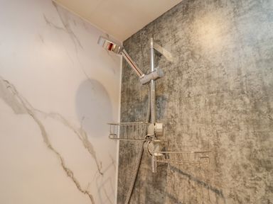 A showerhead with metal wire baskets mounted on a wall with marble and textured gray finishes at Wansfell View in Limefitt Park near Troutbeck