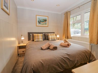 A bedroom with a double bed brown bedding and rolled towels beside a window with yellow curtains at Wansfell View Limefitt Park near Troutbeck