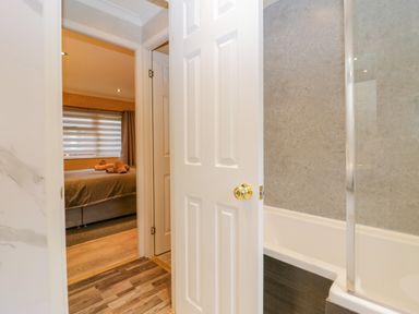 A bathroom with a bathtub and glass shower door looking into a bedroom with a bed and rolled towels at Wansfell View in Limefitt Park near Troutbeck