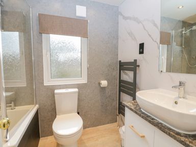A bathroom with a toilet, sink on a vanity, towel radiator, and bathtub with shower at Wansfell View in Limefitt Park near Troutbeck