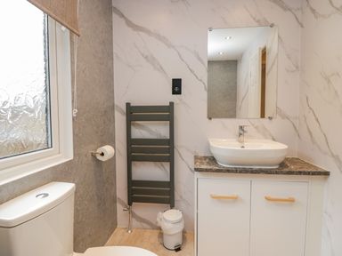 A bathroom with a toilet sink mirror towel rack and a window at Wansfell View in Limefitt Park near Troutbeck