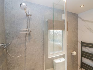 A shower area with a handheld showerhead next to a window and a toilet at Wansfell View in Limefitt Park near Troutbeck