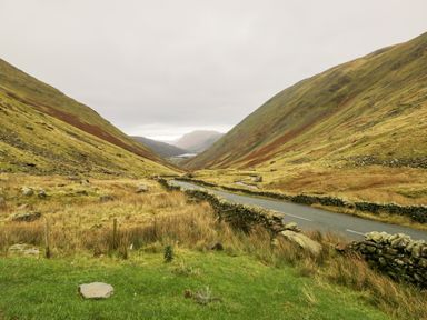 A winding road through a grassy valley between hills with stone walls on both sides at Wansfell View in Limefitt Park near Troutbeck
