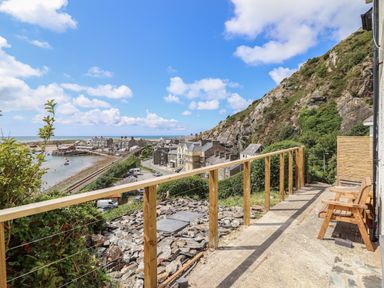 A hillside view with railing and wooden bench overlooking buildings and the sea at Windycroft in Barmouth