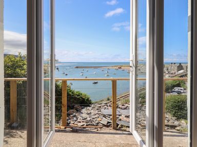 View of a harbor with boats through open glass doors and a wooden railing at Windycroft in Barmouth