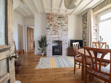 A dining area with wooden chairs and table a brick fireplace and a patterned rug at Windycroft in Barmouth