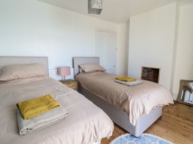 A bedroom with two single beds a nightstand with a lamp a small fireplace and a mirror on the floor at Windycroft in Barmouth