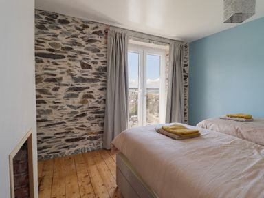 A bedroom with two single beds wooden floor exposed stone wall and double glass doors with curtains at Windycroft in Barmouth