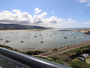 A view of boats on the water with hills in the background and a railway track in the foreground at Windycroft in Barmouth