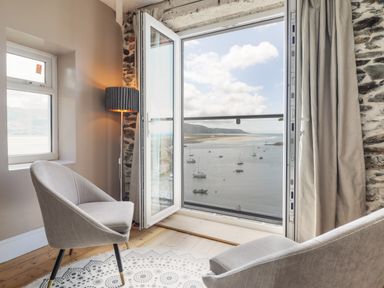 A seating area with two chairs a lamp and an open door overlooking a harbor with boats at Windycroft in Barmouth