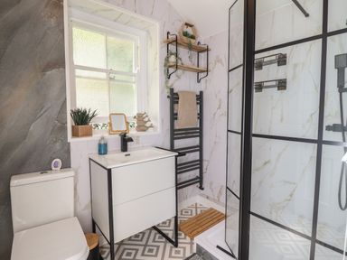 A bathroom with a toilet sink vanity mirror and a shower with glass doors at Windycroft in Barmouth
