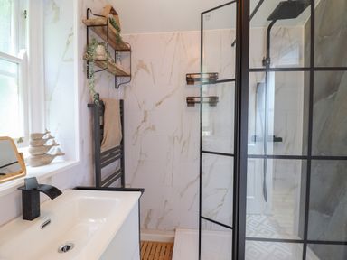 A bathroom with a sink and faucet a black towel rack and a shower with glass panels at Windycroft in Barmouth