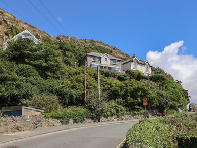 A road with houses on a hillside covered with greenery and a stone wall at Windycroft in Barmouth