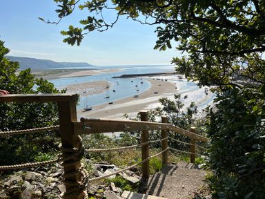 A wooden handrail and steps leading down to a shore with boats anchored in the water at Windycroft in Barmouth