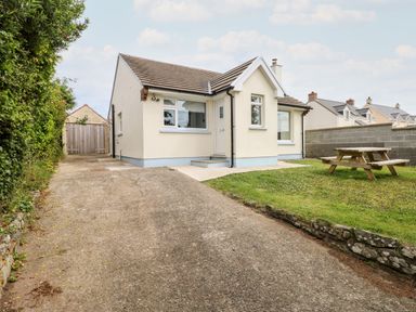 A single story house with a driveway, green lawn, and picnic table at Chalfonts Cottage in Trefin near Penparc