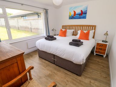 A bedroom with a double bed with orange pillows towels wooden furniture and a large window at Chalfonts Cottage Trefin near Penparc