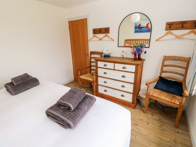 A bedroom with a bed with folded towels wooden chairs a dresser with a mirror and coat hooks on the wall at Chalfonts Cottage in Trefin near Penparc