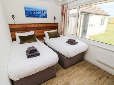 A bedroom with two single beds next to a window showing an outside building at Chalfonts Cottage in Trefin near Penparc