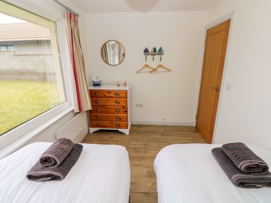 A bedroom with two beds with folded towels a wooden chest of drawers and a round mirror at Chalfonts Cottage in Trefin near Penparc