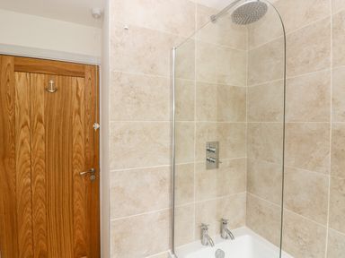 A bathroom with a wooden door and a bathtub with a glass shower screen at Chalfonts Cottage in Trefin near Penparc