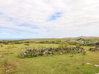 A grassy backyard with a rotary clothesline and stone wall with fields and hills in the distance at Chalfonts Cottage in Trefin near Penparc