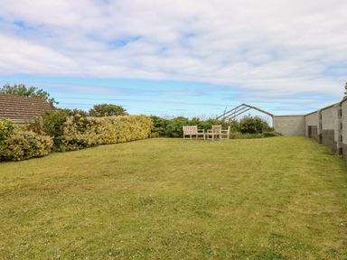 A backyard with green grass bushes wooden chairs and a table near a concrete block wall at Chalfonts Cottage in Trefin near Penparc