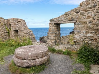 A stone mill wheel and stone ruins with a view of the sea at Chalfonts Cottage in Trefin near Penparc