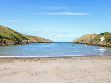 A beach with sand in the foreground and a small bay with boats anchored and hills on both sides at Chalfonts Cottage in Trefin near Penparc