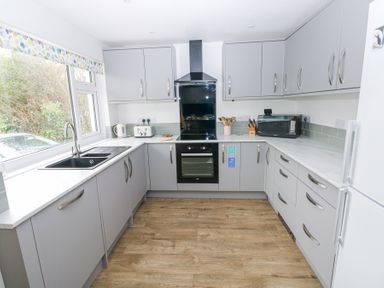 A kitchen with grey cabinets white countertops a black sink oven microwave toaster and kettle at Chalfonts Cottage Trefin near Penparc