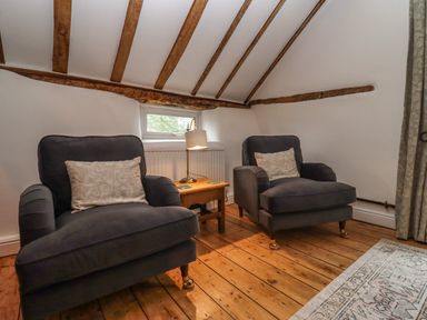 A room with two armchairs separated by a wooden side table with a lamp on a wooden floor with exposed ceiling beams at 1 White House Cottages Bromsash near Lea