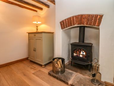 A corner with a wood burning stove under a brick arch and a side cabinet with a lamp at 1 White House Cottages in Bromsash near Lea