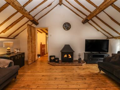 A living room with a wood stove fire a television sofas wooden beams and wooden floor at 1 White House Cottages Bromsash near Lea