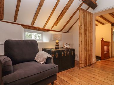 A room with a dark armchair a trunk with a lamp and picture frame wooden floor and ceiling beams at 1 White House Cottages Bromsash near Lea