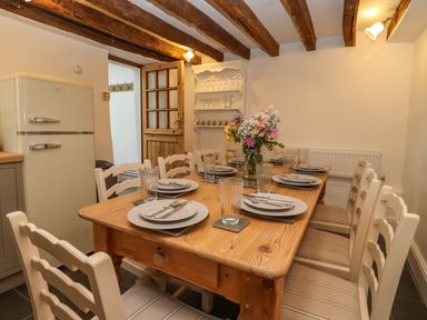 A dining room with a wooden table set for six white chairs and a refrigerator at 1 White House Cottages Bromsash near Lea