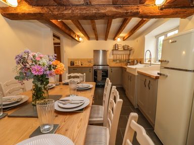 A kitchen with wooden beams a dining table set with plates and glasses and a vase of flowers at 1 White House Cottages Bromsash near Lea