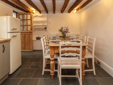 A dining room with a wooden table set with plates glasses and a flower vase surrounded by white chairs at 1 White House Cottages Bromsash near Lea