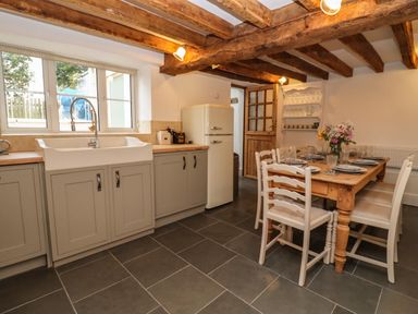A kitchen with a dining table set with plates and glasses exposed wooden beams and a window above a sink at 1 White House Cottages Bromsash near Lea
